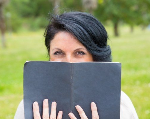 Woman covering her smile with black book