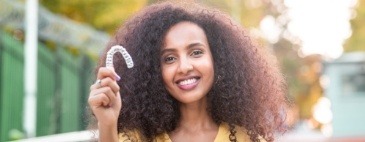 Smiling woman holding clear aligner outdoors
