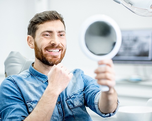 Bearded man checking smile in handheld mirror