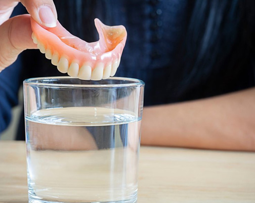 Close up of patient dropping their denture into a cleaning solution