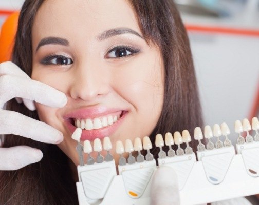 Young woman smiling while cosmetic dentist fits her with dental veneers