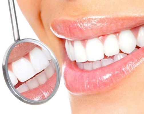 Close up of dental mirror reflecting smile with white teeth