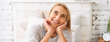 Smiling woman in white sweater resting her chin in her hands and looking up