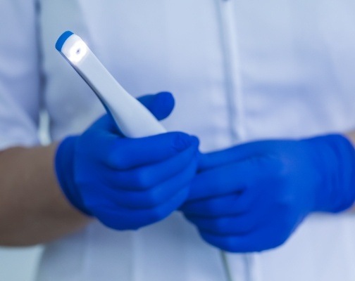 Two gloved hands holding a thin white intraoral camera