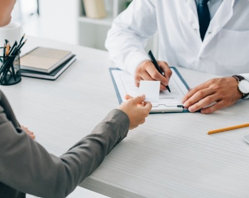 Woman handing payment card to dentist across desk