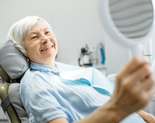 Senior dental patient admiring her smile in mirror