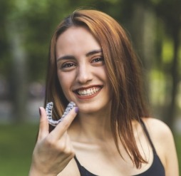 Smiling young woman holding Invisalign clear aligner outdoors