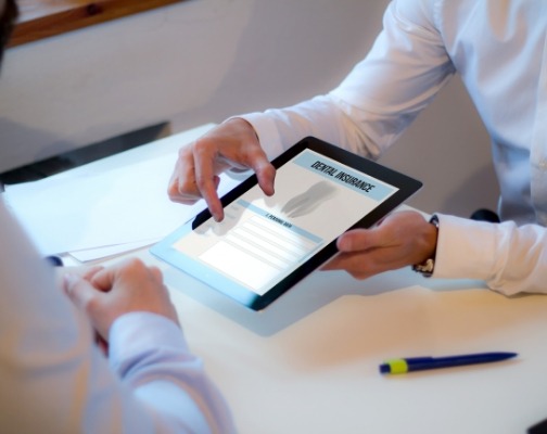 Two people sitting across from each other at desk looking at dental insurance forms on a tablet