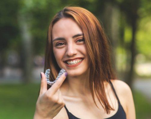 Smiling young woman holding Invisalign clear aligner outdoors