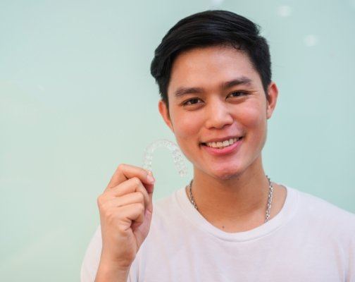 Smiling young man holding Invisalign tray