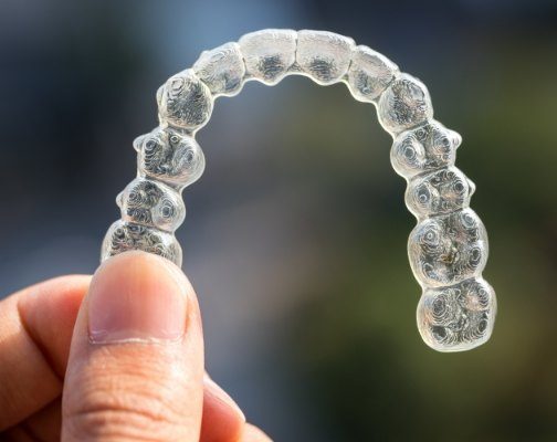 Hand holding a clear Invisalign aligner