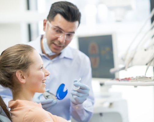 Dentist showing Invisalign trays to a young woman in dental chair