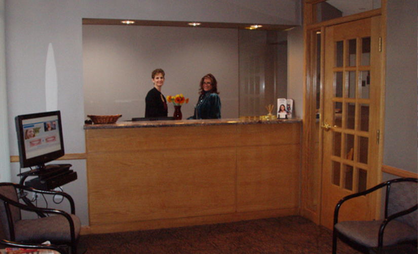 Two smiling dental team members standing behind front desk at Boston Smile Center