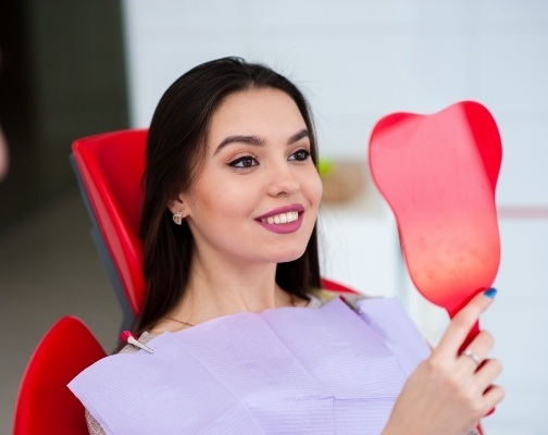 Young woman admiring her teeth in mirror after smile makeover in Brookline