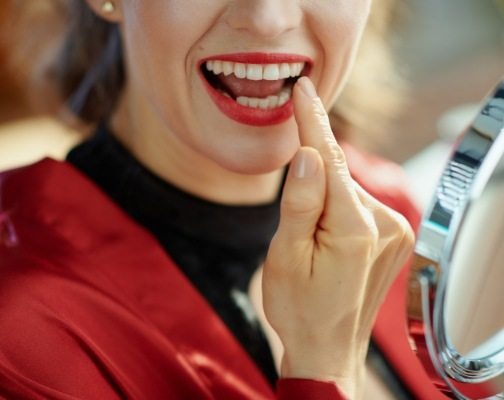 Woman with red lipstick looking at her teeth in mirror