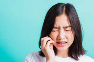 Woman with braces holding face in discomfort on blue background