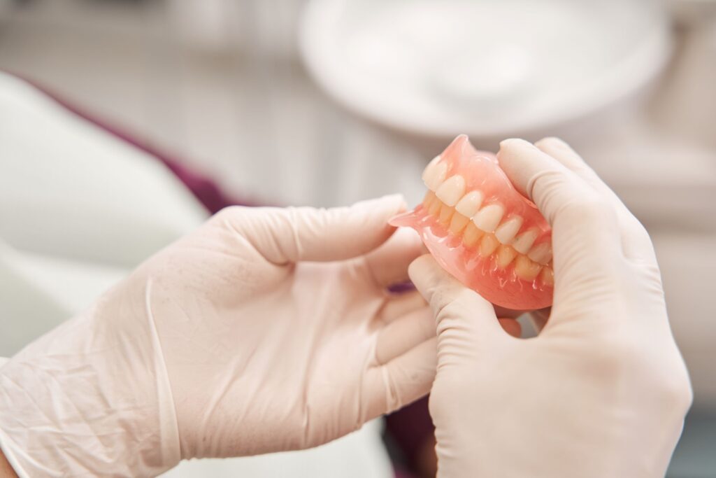 Gloved hands holding full set of shiny dentures