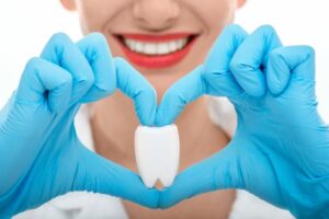 Woman holding tooth with hands in heart shape.