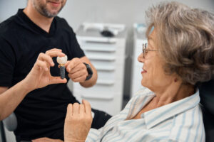 Patient examines model of dental implant in hands of dental prosthetist, the doctor consults her at an appointment