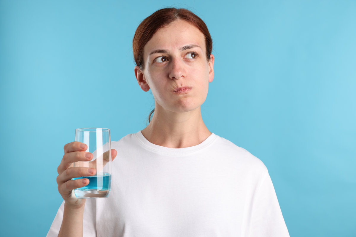 Woman rinsing mouth with mouthwash on light blue background