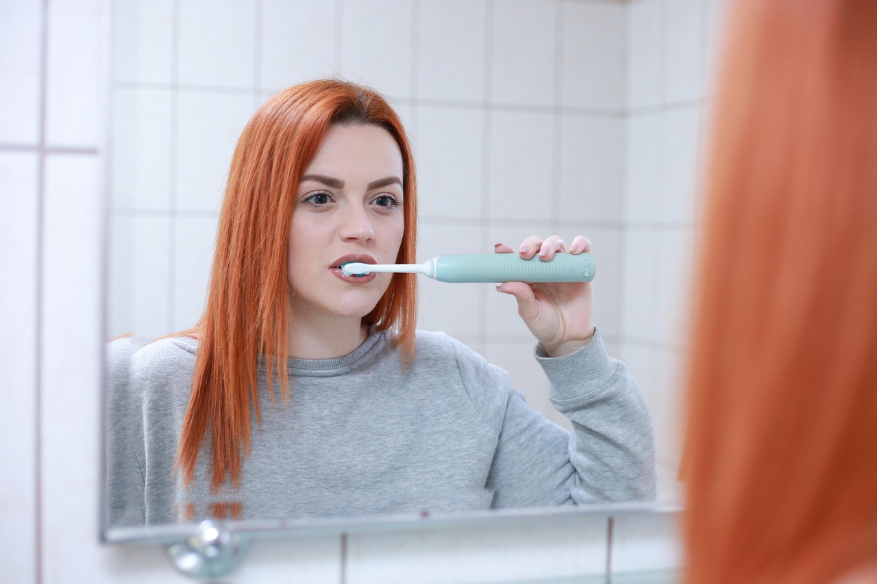 Person brushing teeth with an electric toothbrush, maintaining daily oral hygiene to care for dental implants
