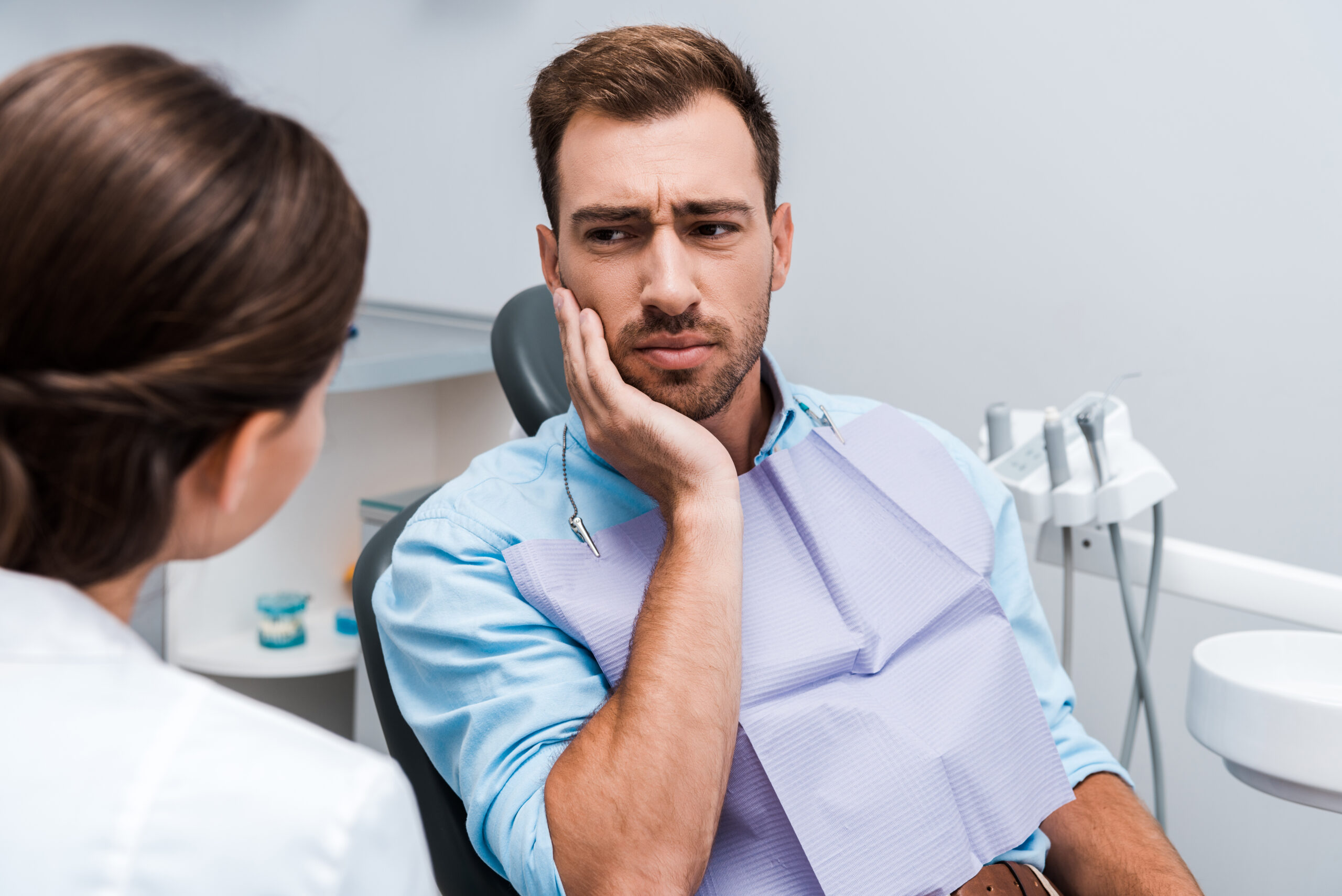 Patient experiencing dental emergency pain touching face near dentist
